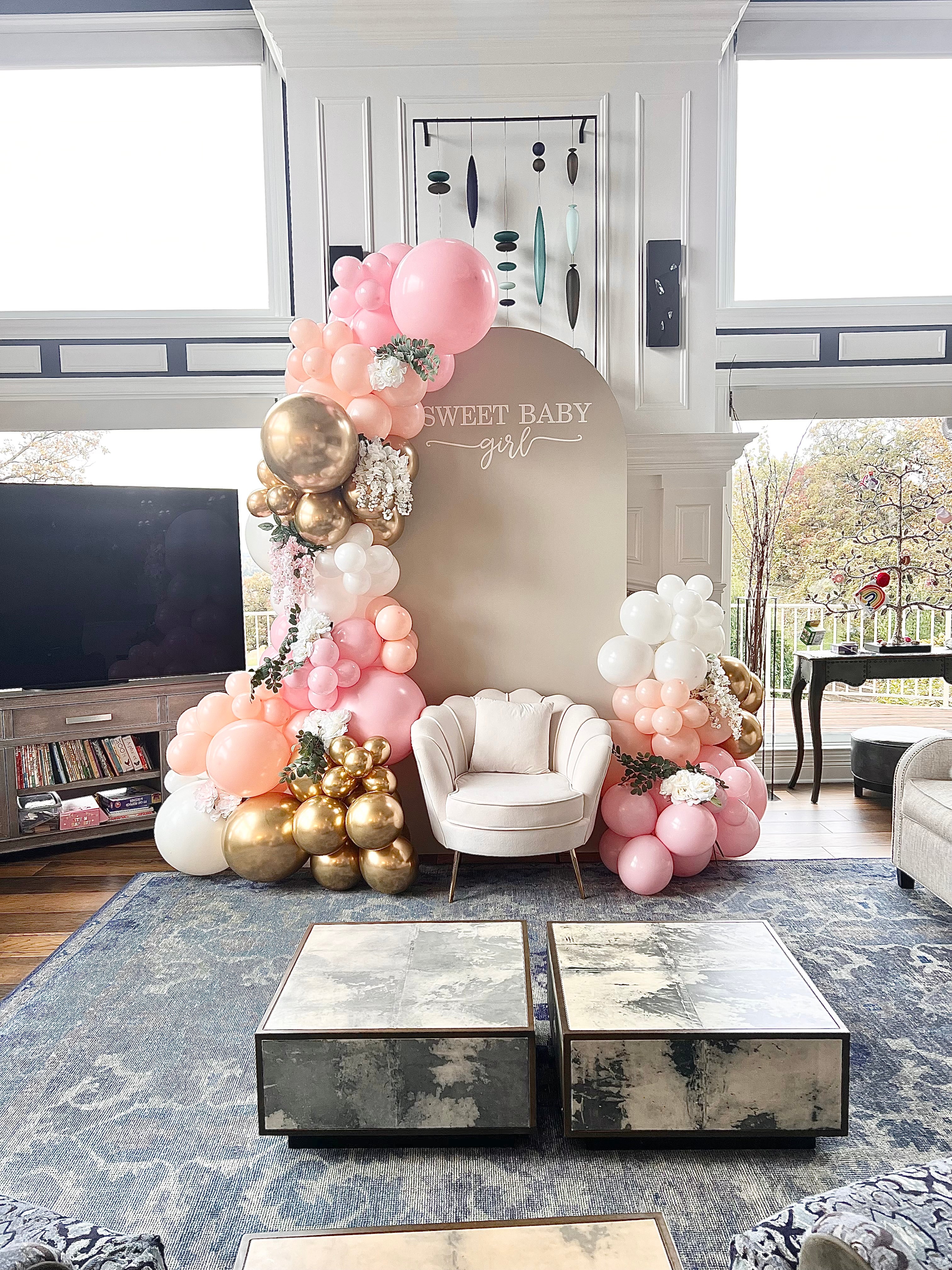 Pink peach white and gold baby shower balloons with an arch backdrop and guest of honor chair